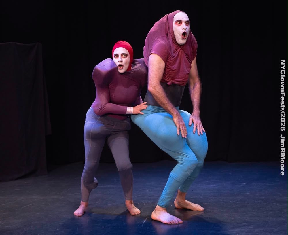 One performer grips the hips of the other from behind, both gasping in surprise.