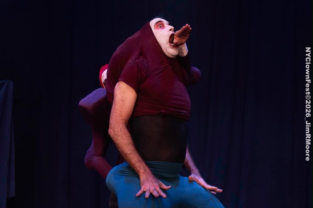 The tall bouffon throws his head back with a hand at his open mouth.